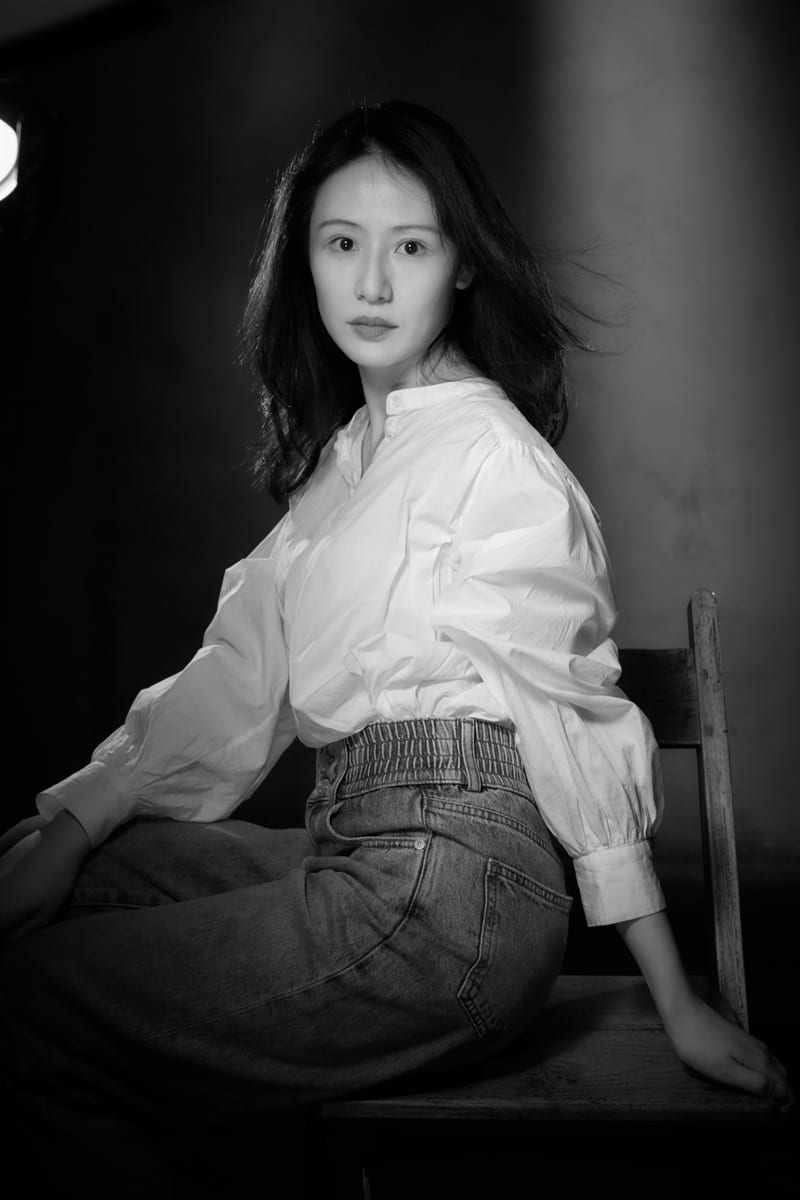 黑白肖像：女性坐在墙边，双手交叠